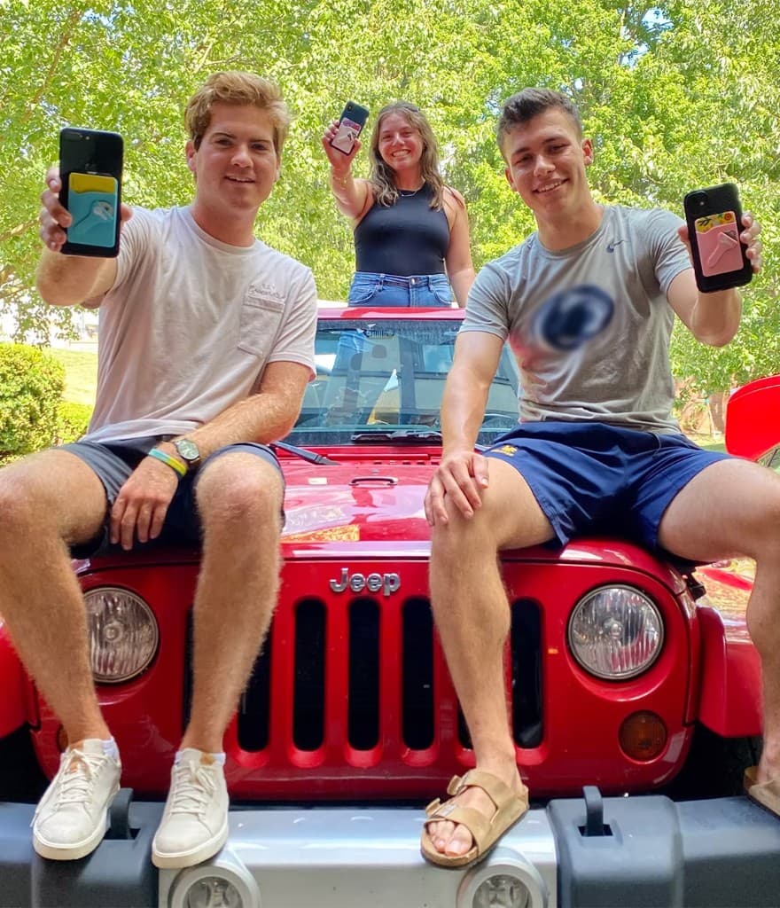 The Keyper team holding up early Keyper phone wallets on the hood of a red Jeep.